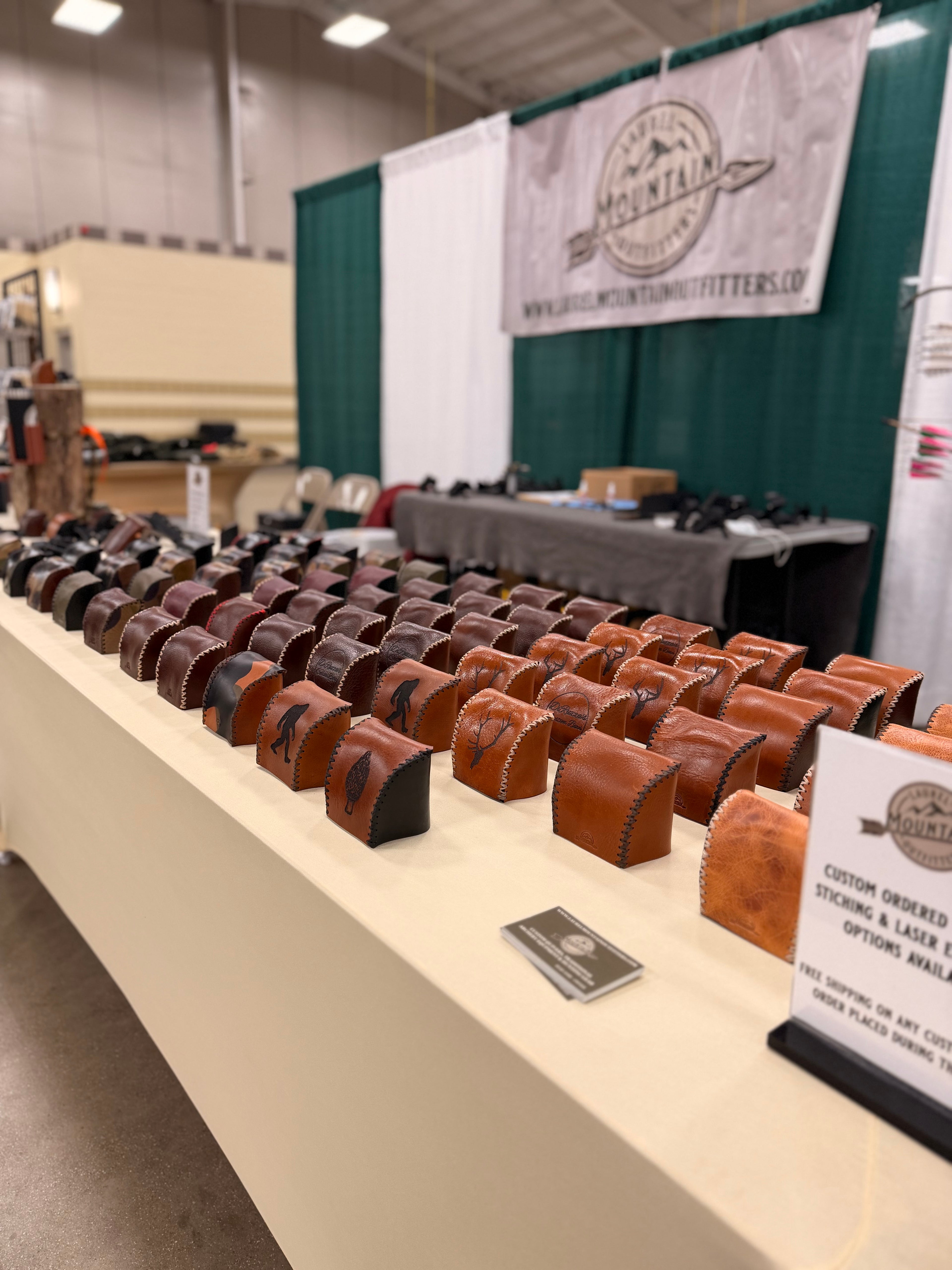 Row of leather products on a table with a branded backdrop at an event.